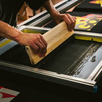 黒Tシャツに黒インキをスキージーで塗る職人の手元の写真