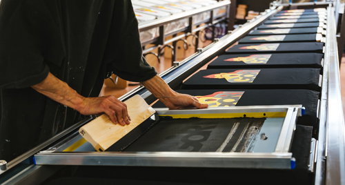 ズラリと並んだTシャツに手刷りで着色していく職人