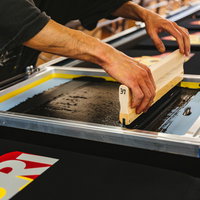 オレンジ色のスキージーを使って版を手刷りするTシャツ工程の写真