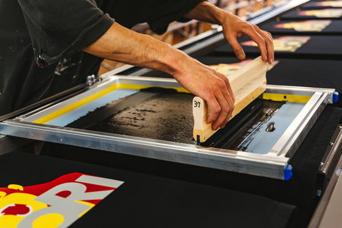 オレンジ色のスキージーを使って版を手刷りするTシャツ工程