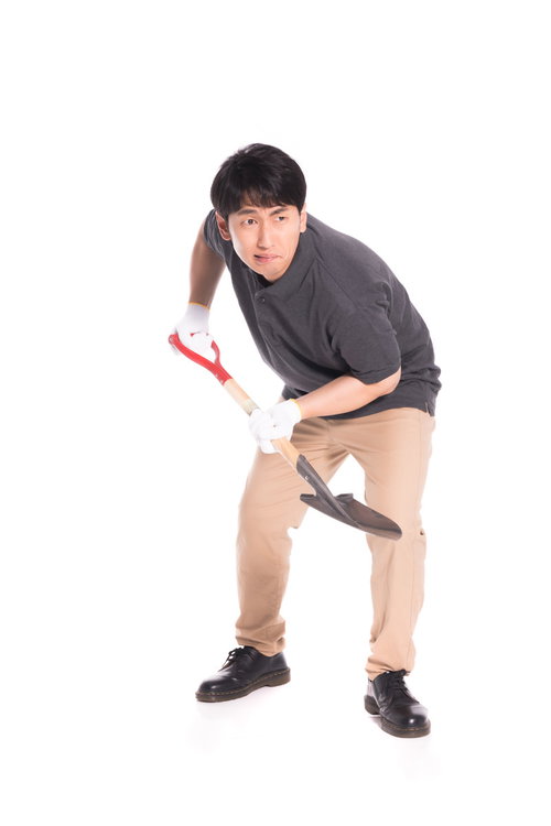 赤いシャベルで地面を掘り起こす男性