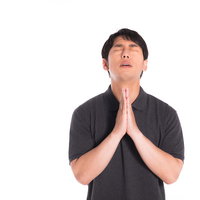 黒いポロシャツを着て目を閉じて合掌する男性の写真