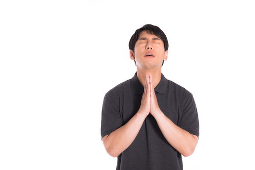 黒いポロシャツを着て目を閉じて合掌する男性