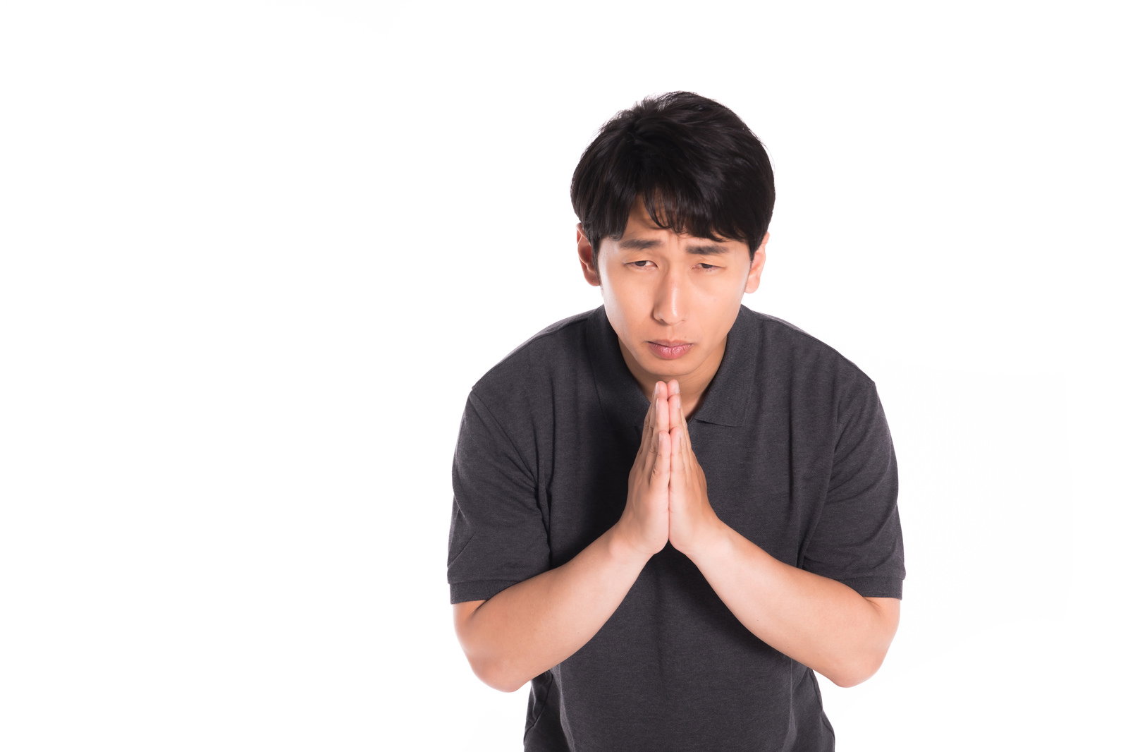 黒いTシャツを着た男性が両手を合わせて謝罪している様子［モデル：大川竜弥］