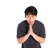 手を合わせて平謝りする黒いTシャツの男性の写真