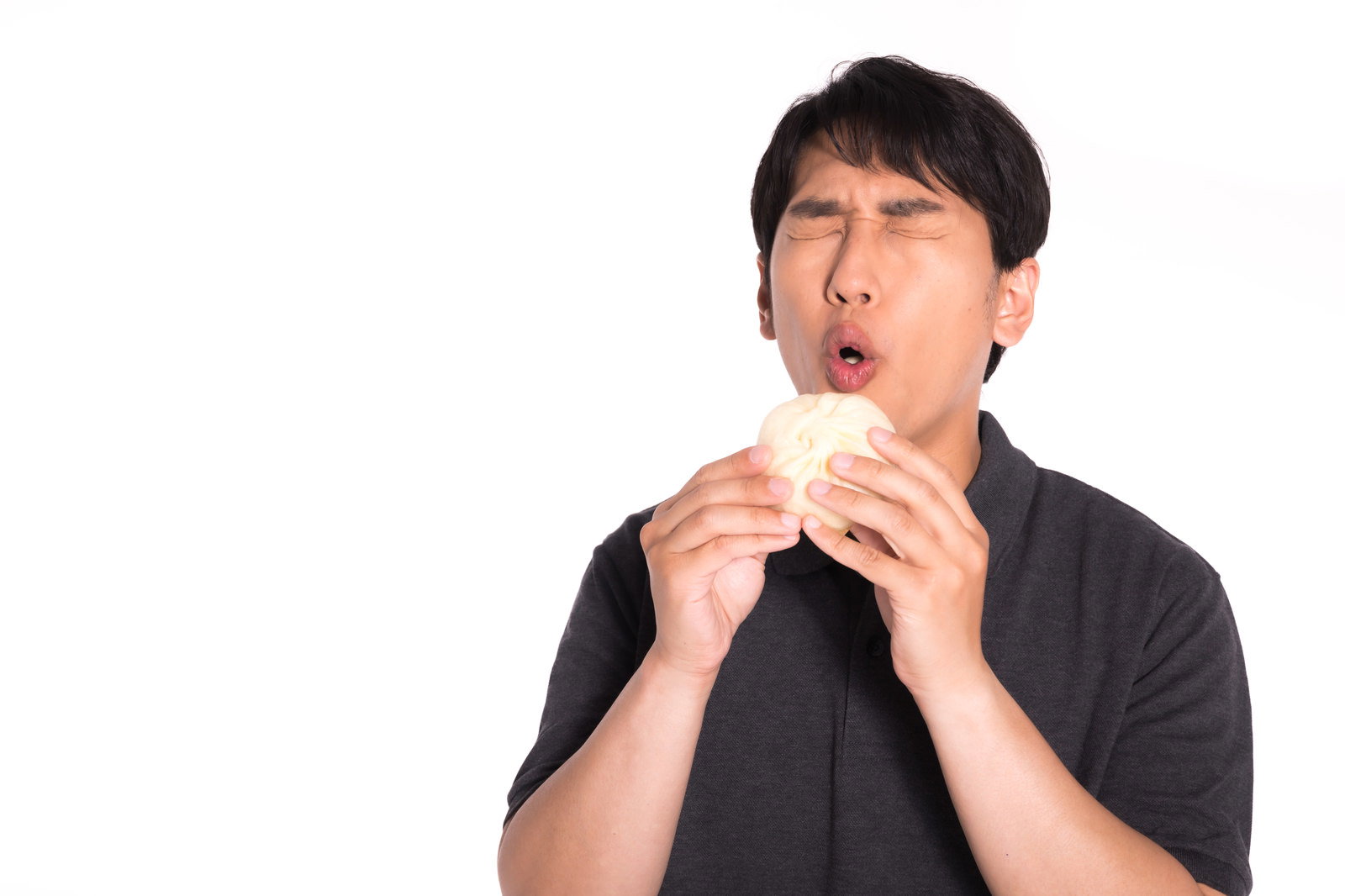アツアツの肉まんを手に持って美味しそうに頬張る男性［モデル：大川竜弥］