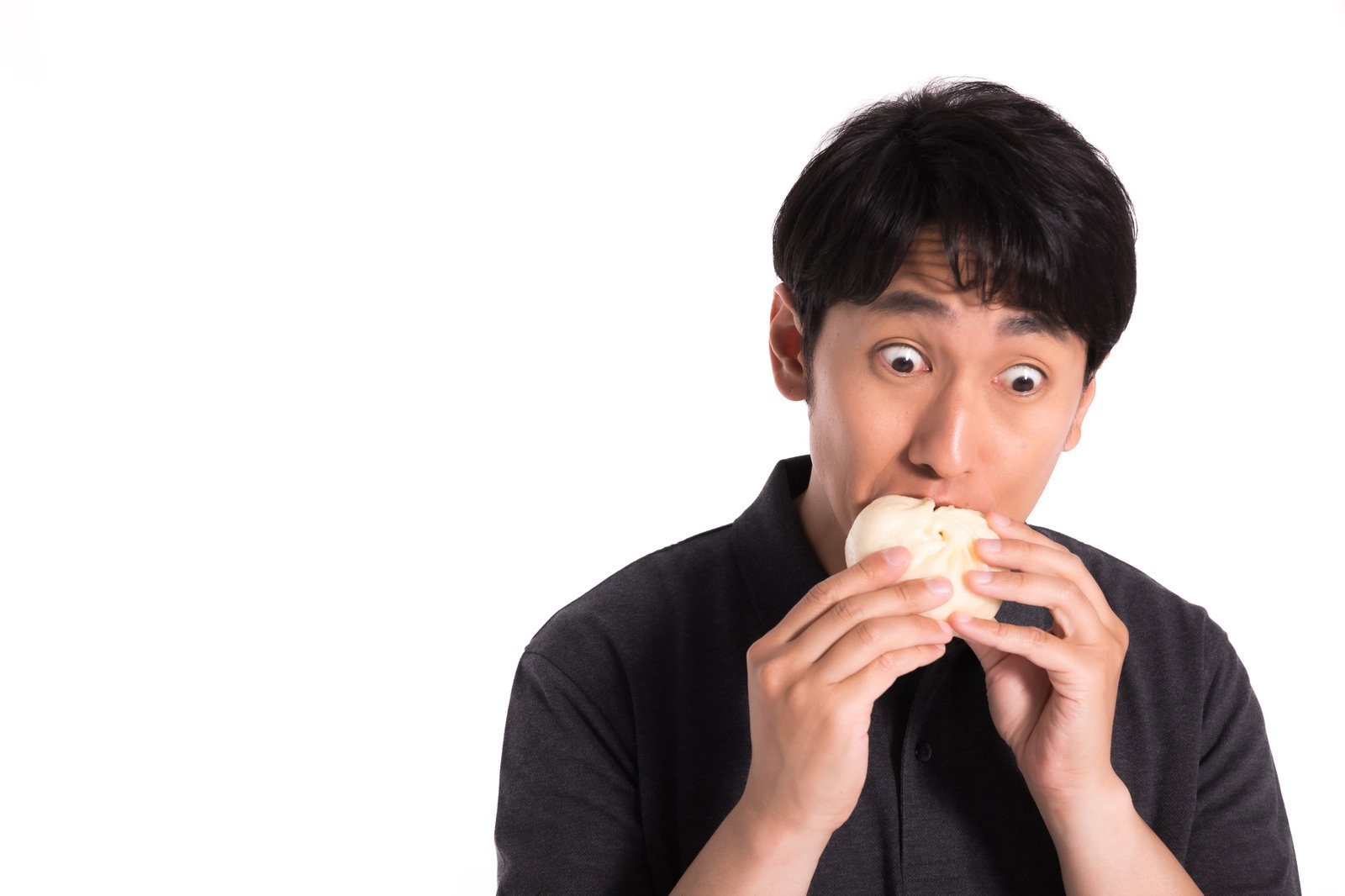白い豚まんを両手で持ち、驚いた表情で食べている黒シャツの男性［モデル：大川竜弥］