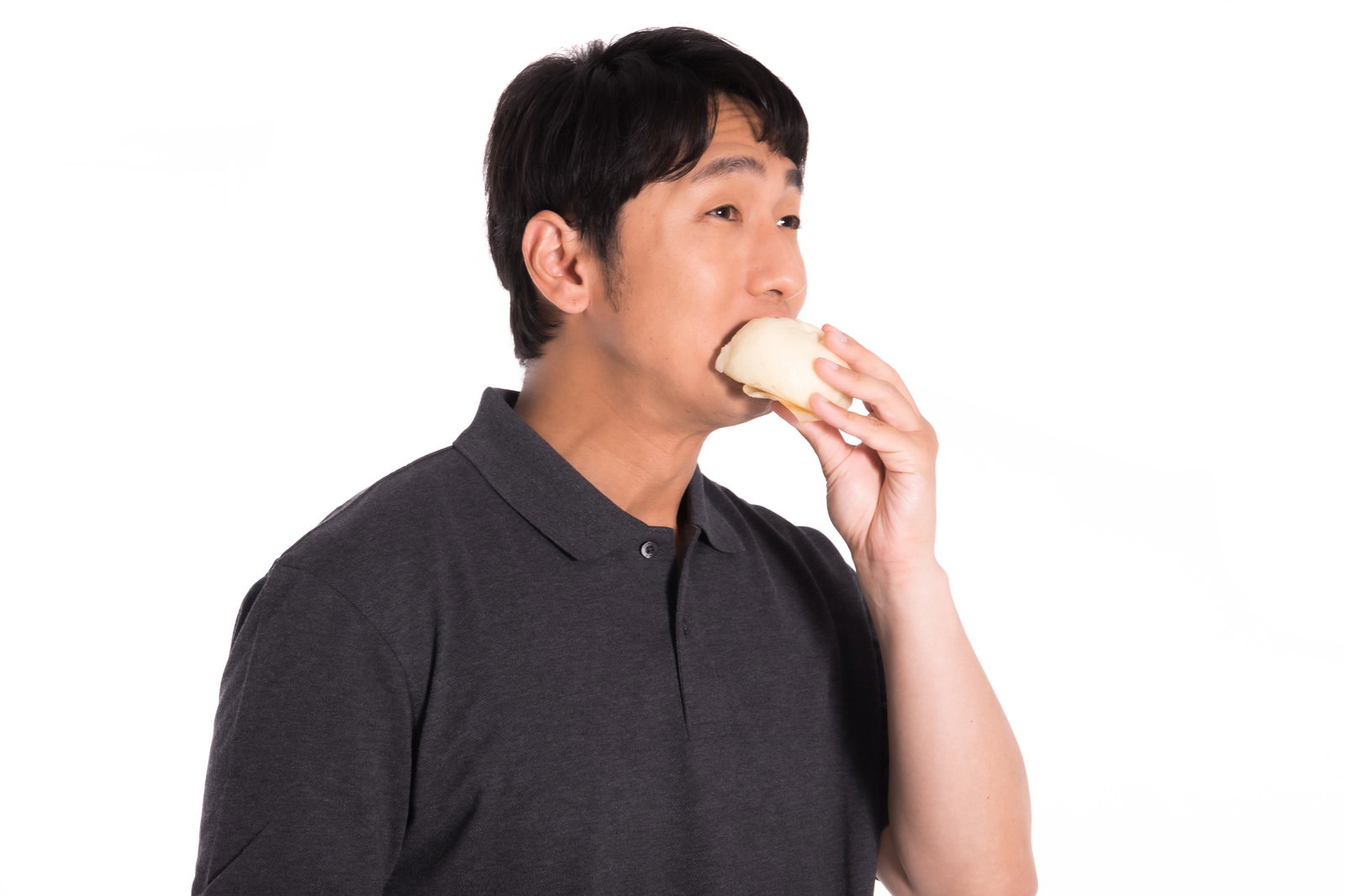 グレーのパーカーを着た男性が白い背景で豚まんを片手に持って食べている様子［モデル：大川竜弥］