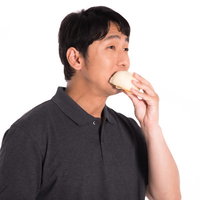 片手で豚まんを食べる男性、グレーのパーカー姿で白背景の写真