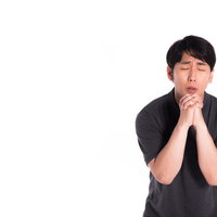ぶつぶつと反省の意を述べて手を合わせる男性の写真