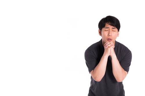 ぶつぶつと反省の意を述べて手を合わせる男性