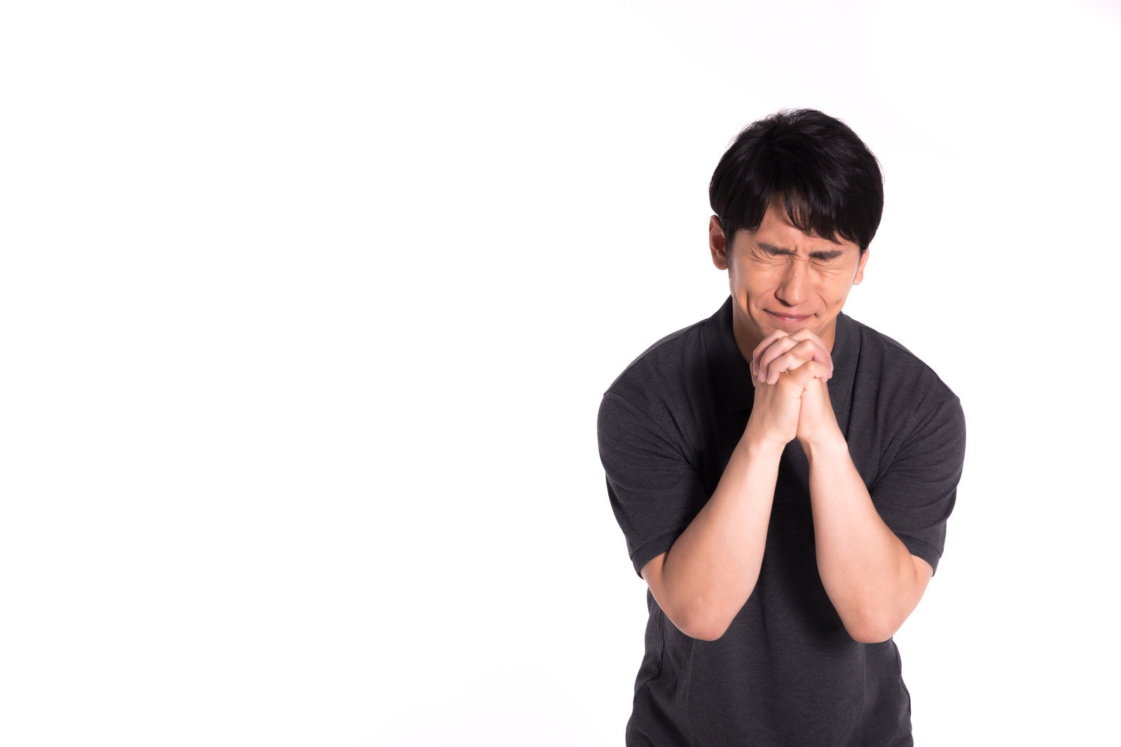 黒いTシャツを着た男性が両手を合わせて目を閉じて祈っている［モデル：大川竜弥］