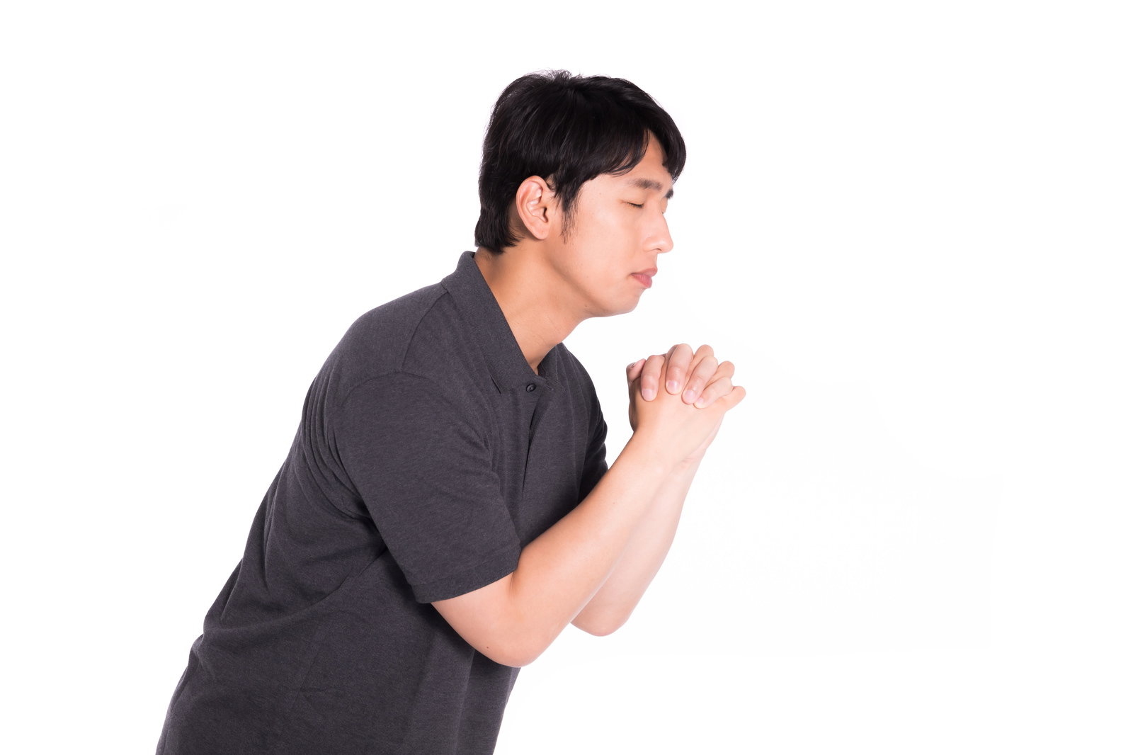グレーのシャツを着た男性が両手を合わせて目を閉じ、真剣に祈りを捧げている様子［モデル：大川竜弥］