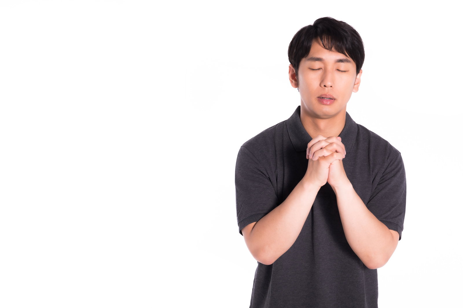 黒いTシャツを着た男性が目を閉じて両手を胸の前で合わせて祈っている［モデル：大川竜弥］