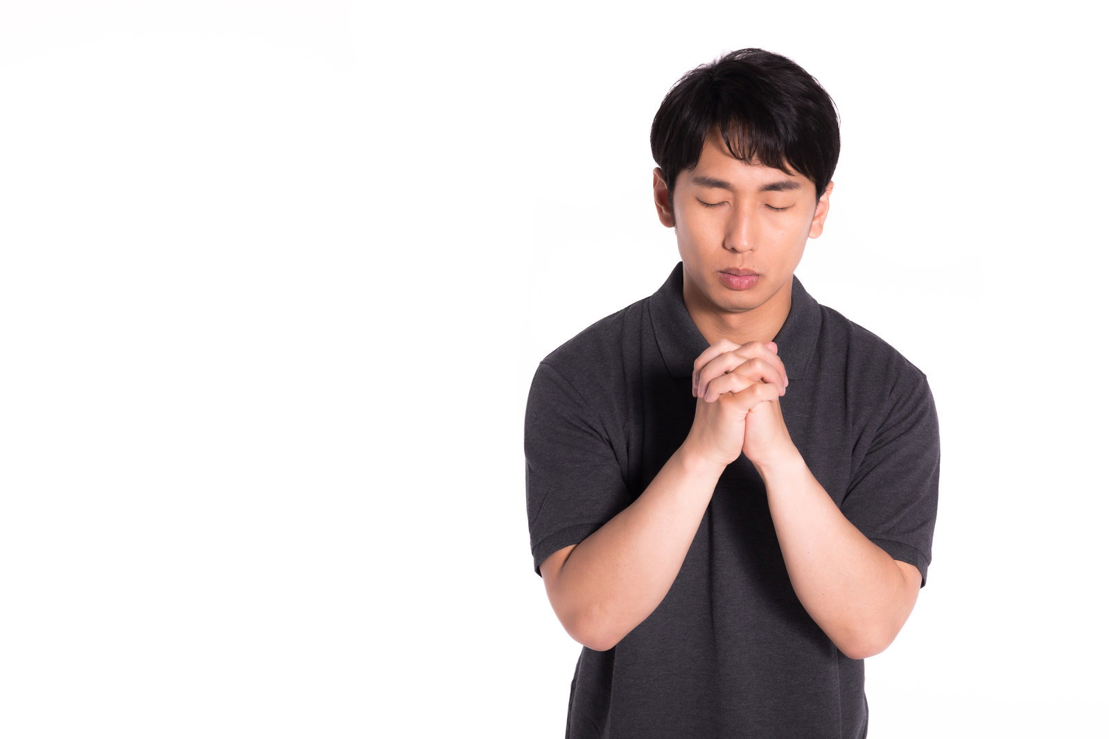 黒いシャツを着た男性が両手を合わせて祈っている様子［モデル：大川竜弥］