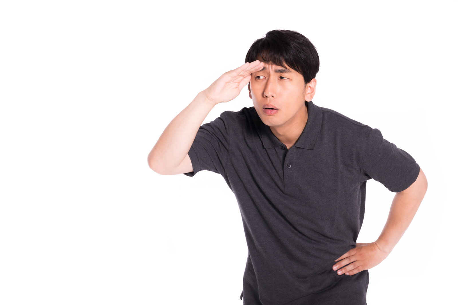 手を額に当てて遠くを見つめ、何かを確認している黒髪の男性［モデル：大川竜弥］