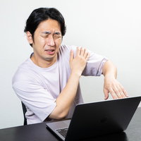 腕の違和感を覚えながらデスクワークを続ける男性の写真