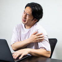 腕の張りが気になるデスクワーク中に肩を回す男性の写真