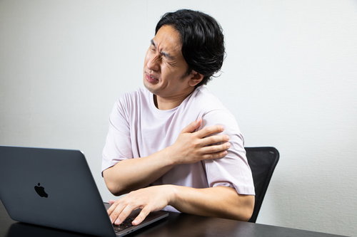 腕の張りが気になるデスクワーク中に肩を回す男性