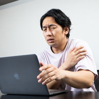 片腕を抑えて肩の痛みでしかめっ面の男性デスクワーカーの写真
