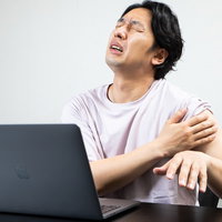 ワクチン接種後の左腕の痛みに耐えるリモートワーク中の男性の写真