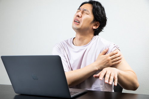 ワクチン接種後の左腕の痛みに耐えるリモートワーク中の男性