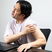 デスクワークで左腕の様子がおかしい男性、肩の痛みで苦しむの写真