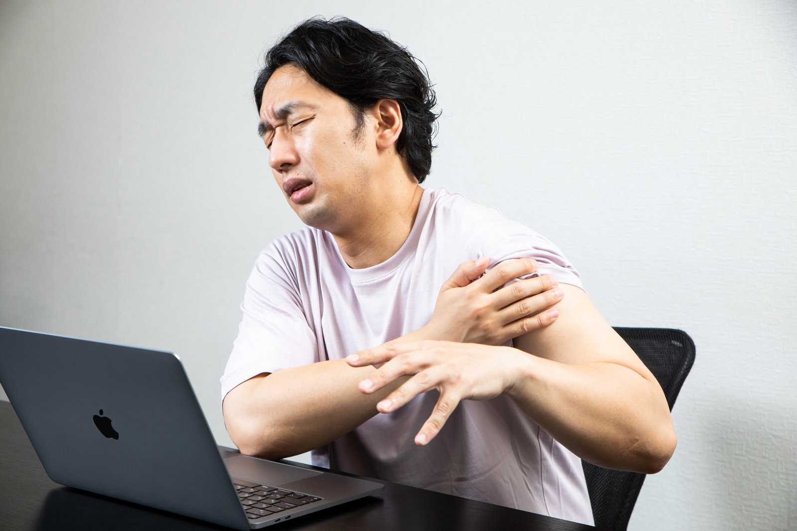 パソコンの前で肩を押さえて痛そうな表情をする男性［モデル：大川竜弥］