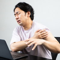 ワクチン接種後に腕の痛みを感じてしかめっ面をする男性の写真