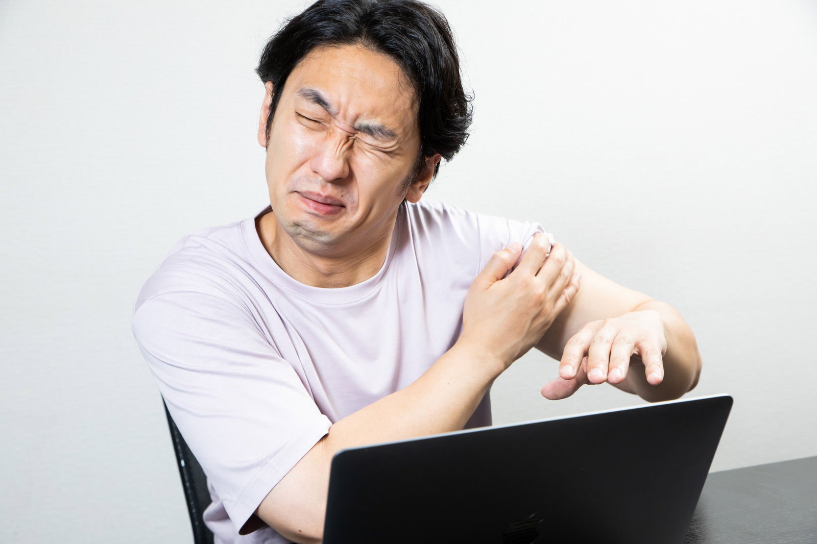 パソコンの前で肩を押さえながら痛そうな表情をする男性［モデル：大川竜弥］