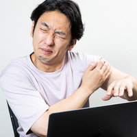 連投で腕が回らず困惑するデスクワーク中のエンジニア男性の写真