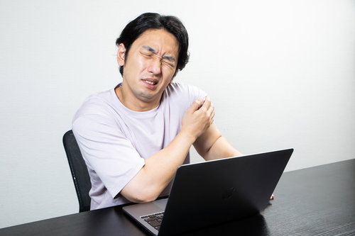 腕の痛みを我慢してデスクワークするしかめっ面の男性