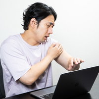 ワクチンを接種した腕の痛みが消えず仕事が手につかない男性の写真