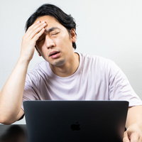 デスクワーク中に頭痛を我慢する男性の疲労とストレスの写真