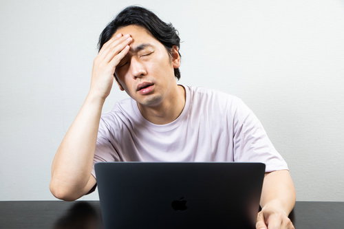 デスクワーク中に頭痛を我慢する男性の疲労とストレス