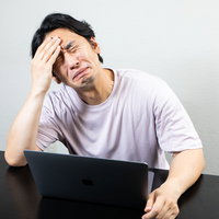 偏頭痛の痛みを我慢しながらデスクワークを続ける男性の写真