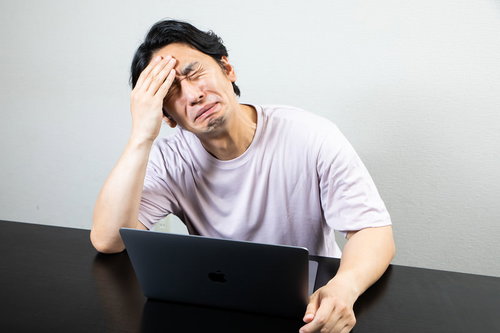 偏頭痛の痛みを我慢しながらデスクワークを続ける男性