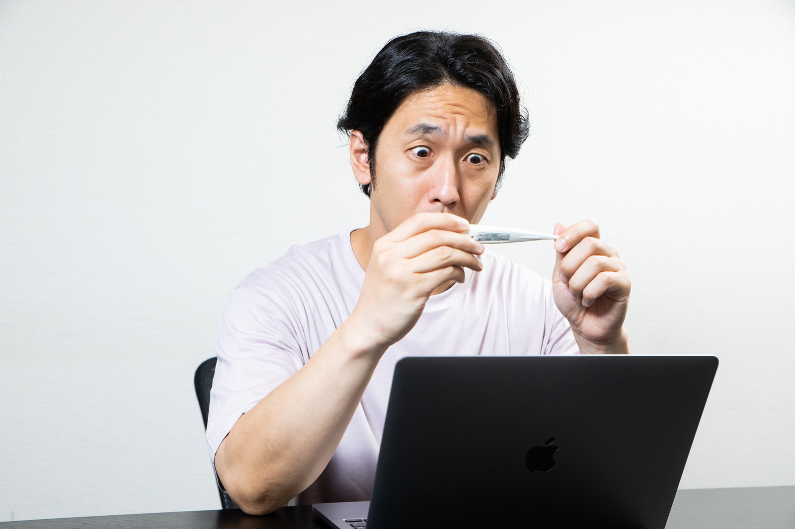 白いシャツの男性が体温計を手に持ち数値を確認している［モデル：大川竜弥］