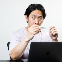 デスクワーク中に体温計の表示を目を凝らして確認する男性の写真