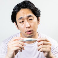 体温計を眺めてうなだれる男性の発熱時の表情の写真
