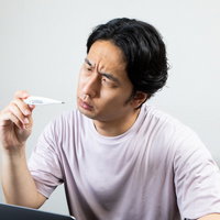 体温計の数値を凝視してしかめっ面になる男性の写真