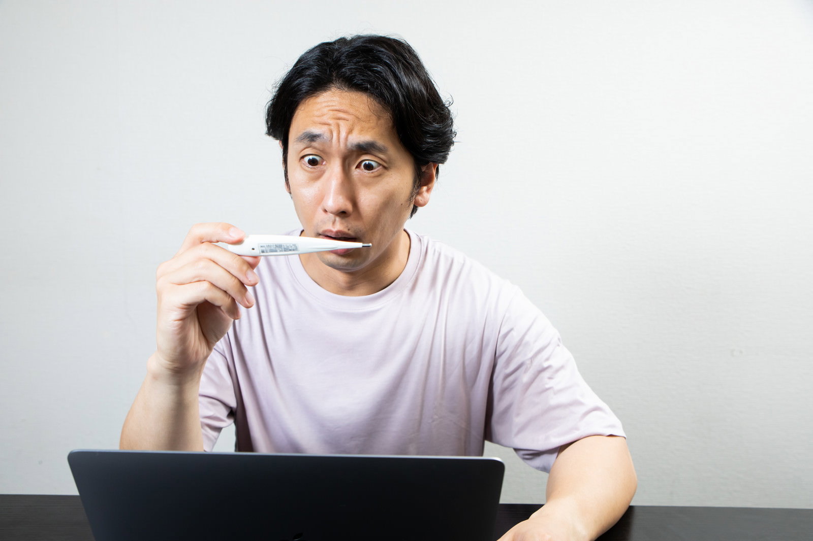 体温計を持って驚いた表情を見せる白いTシャツの男性［モデル：大川竜弥］