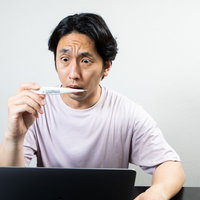 体温計を二度見する男性のデスクワーク中の表情の写真