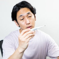 副反応の発熱でボーっとうなだれる男性の体調不良の写真