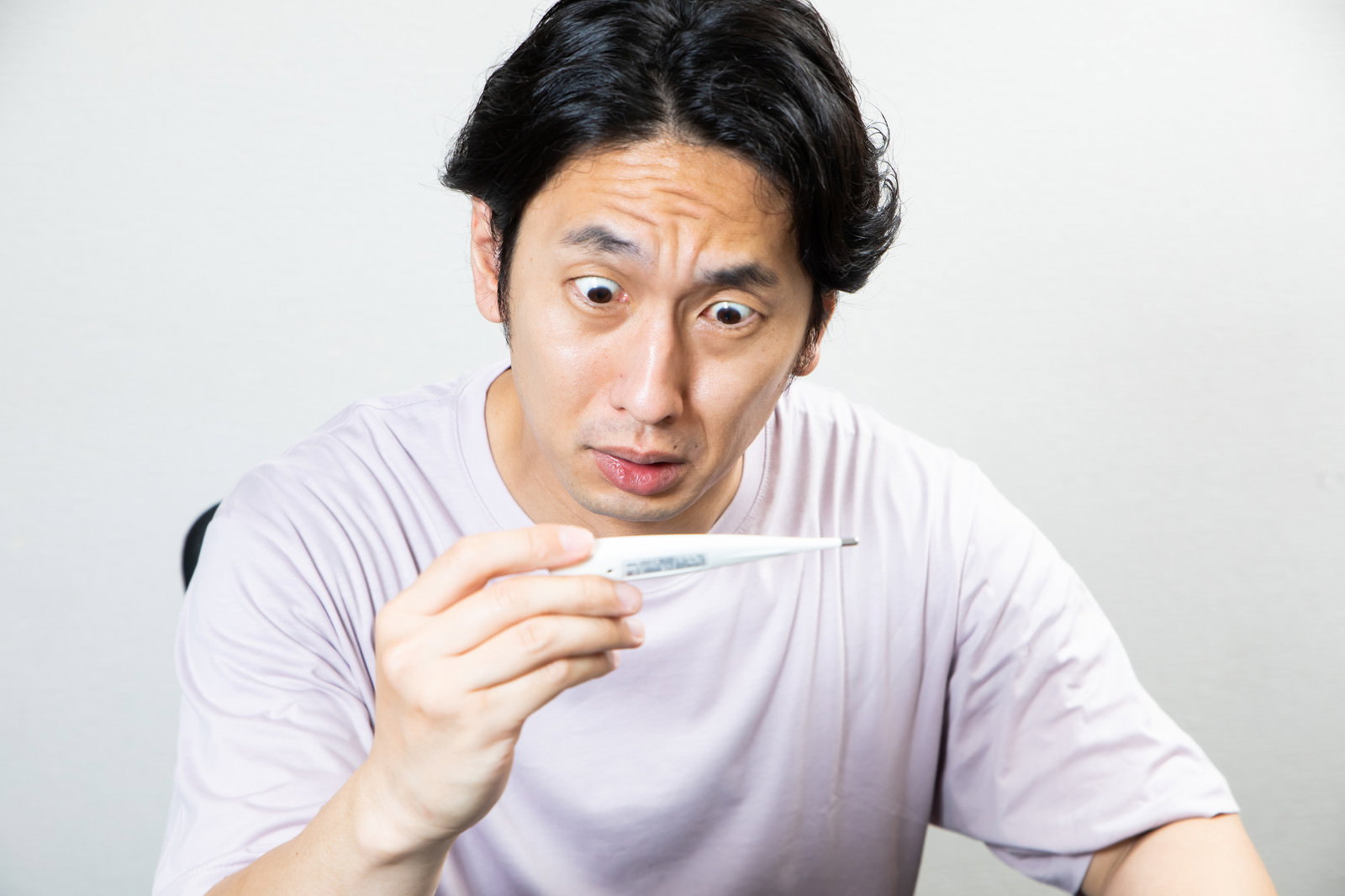 体温計を手に持ち驚いた表情を浮かべる男性［モデル：大川竜弥］