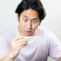 体温計を見て平熱の低さに驚愕する男性の写真