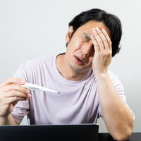 微熱が続く中、デスクワークをする男性の体調管理の写真