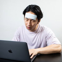 リモートワーク中に風邪で体調不良になりぐったりしている男性の写真