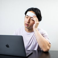 おでこを冷やしながら在宅ワークする男性の頭痛対策の写真