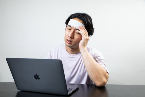 おでこを冷やしながら在宅ワークする男性の頭痛対策